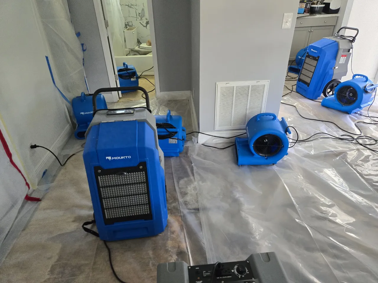 Dehumidifiers and air movers running behind plastic containment during water mitigation